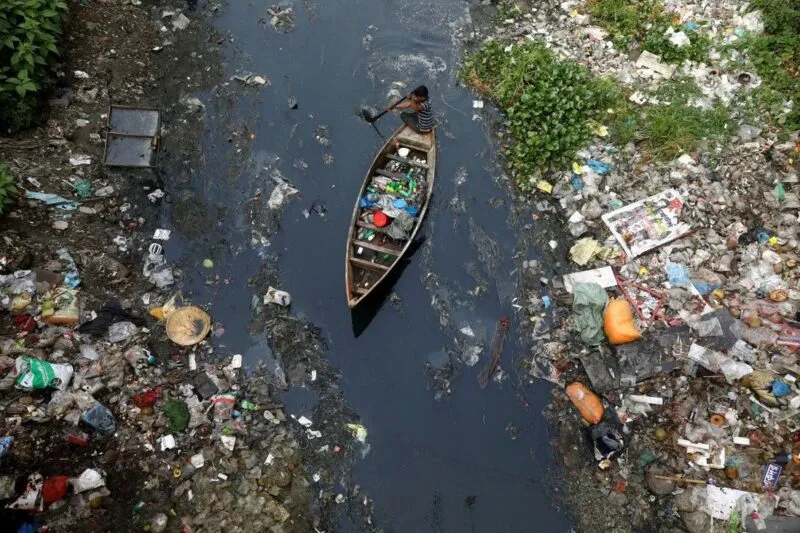 Kleines Boot auf einem stark mit Kunststoffabfällen verschmutzten Fluss mit Abfallansammlungen an den Ufern