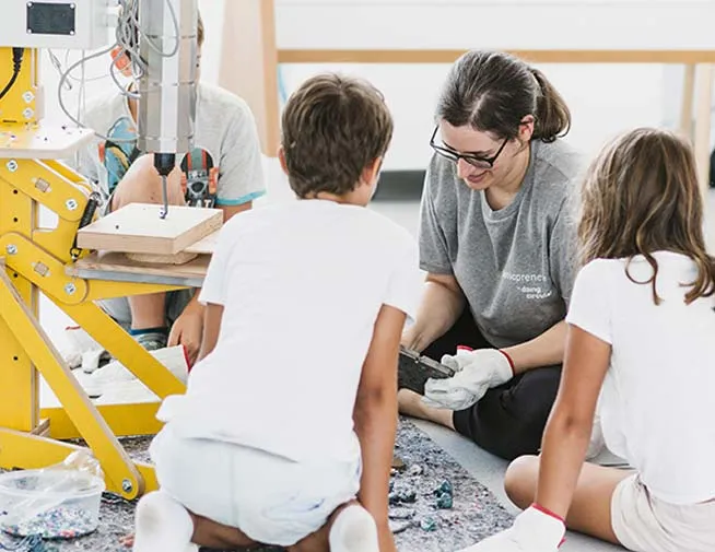 Facilitator showing recycled plastic fragments to two children beside workshop equipment