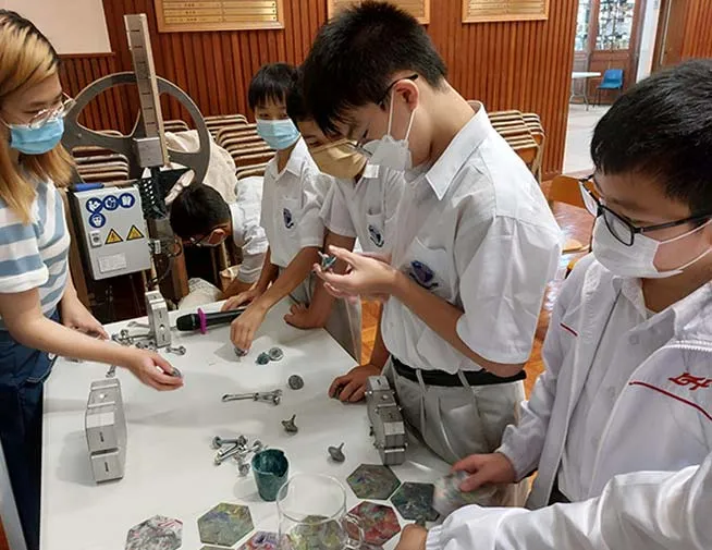 Students examining small objects beside plastic recycling equipment