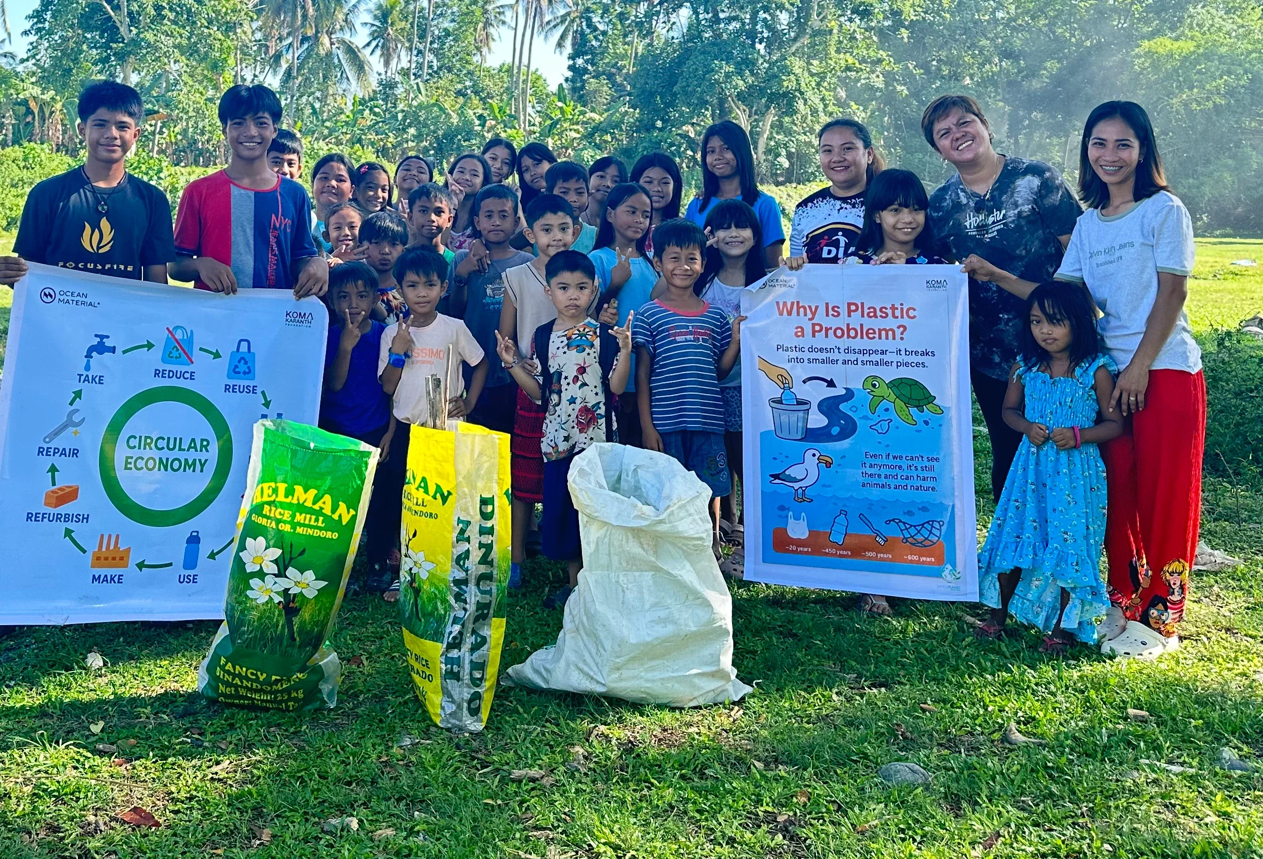Children and adults holding circular economy and plastic pollution posters at a community workshop in the Philippines